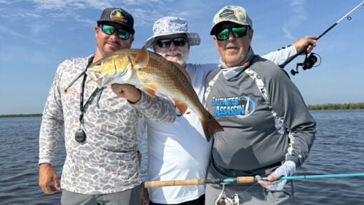 Three Anglers on a boat holding a Redfish