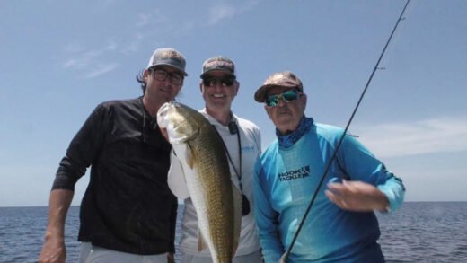 Three anglers proudly displaying large redfish caught artificial bait fishing