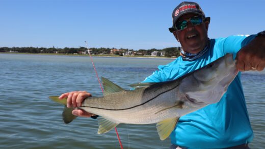 Captain Sergio Atanes in bright blue fishing shirt and Yamaha cap holding a large snook