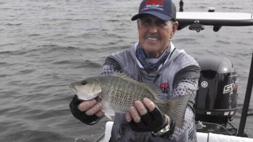 Captain Sergio Atanes holding a mango snapper on Tampa Bay with fishing rod and boat visible in background