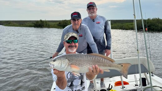 Angler holding a redfish in Louisiana marshes with guides on a Hopedale fishing boat